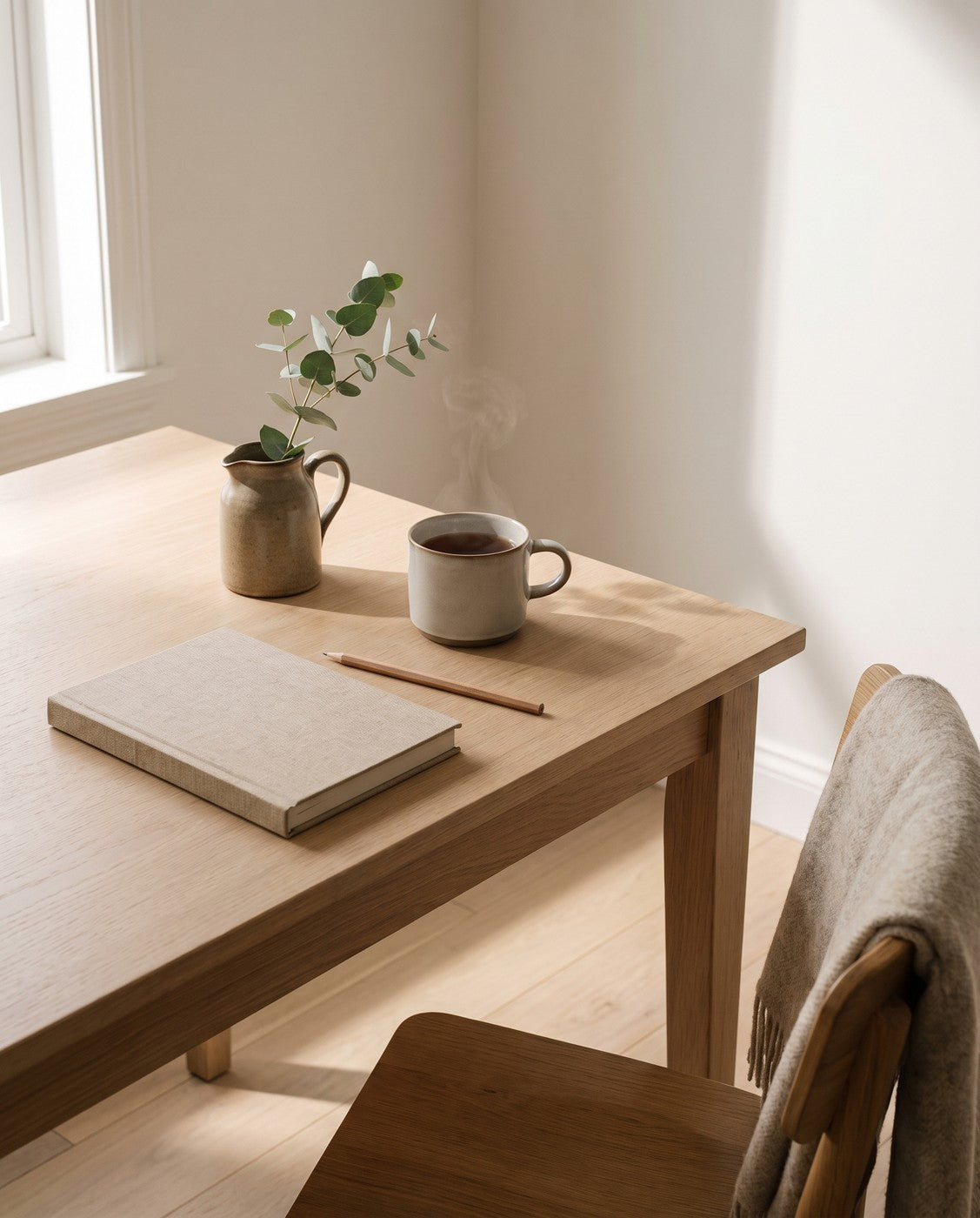 A notebook, pencil and mug of tea on a sunlit kitchen table