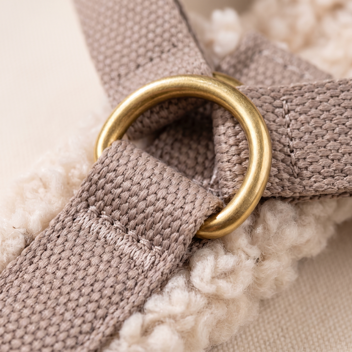 Close up of the brass-coloured D-ring bar tacked onto the taupe webbing